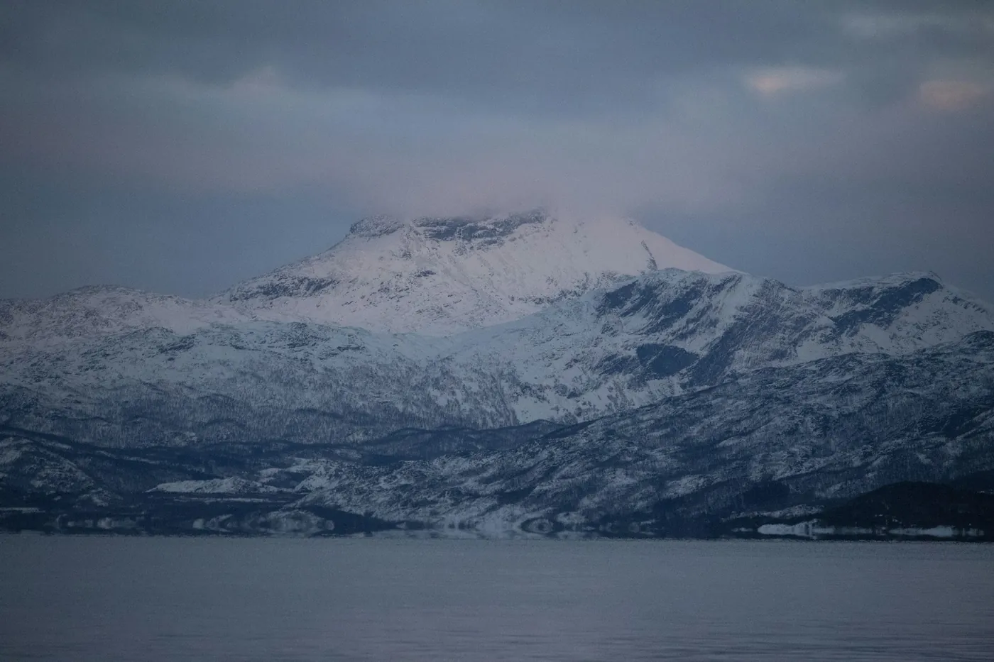 Montagnes enneigées de l’autre côté d’un fjord sombre à Narvik, sous d’épais nuages gris