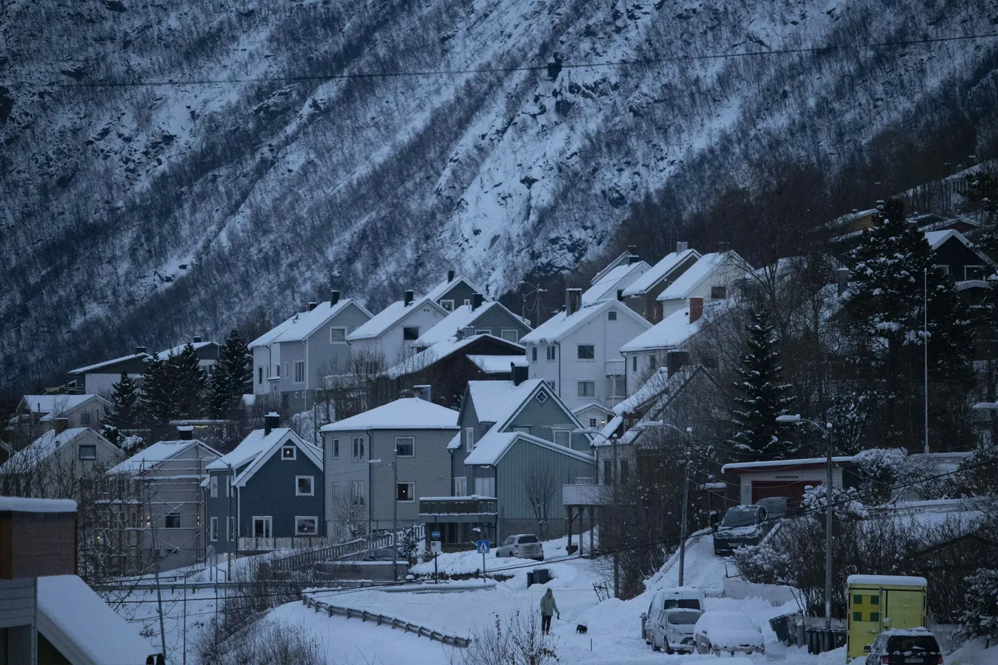Case di legno su una strada in pendenza innevata a Narvik, sotto una ripida parete di montagna striata di neve