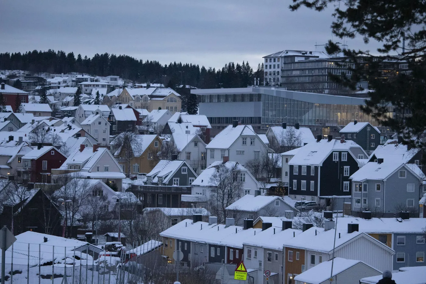 Toits enneigés de Narvik sur le versant, avec un bâtiment moderne en verre et des immeubles derrière